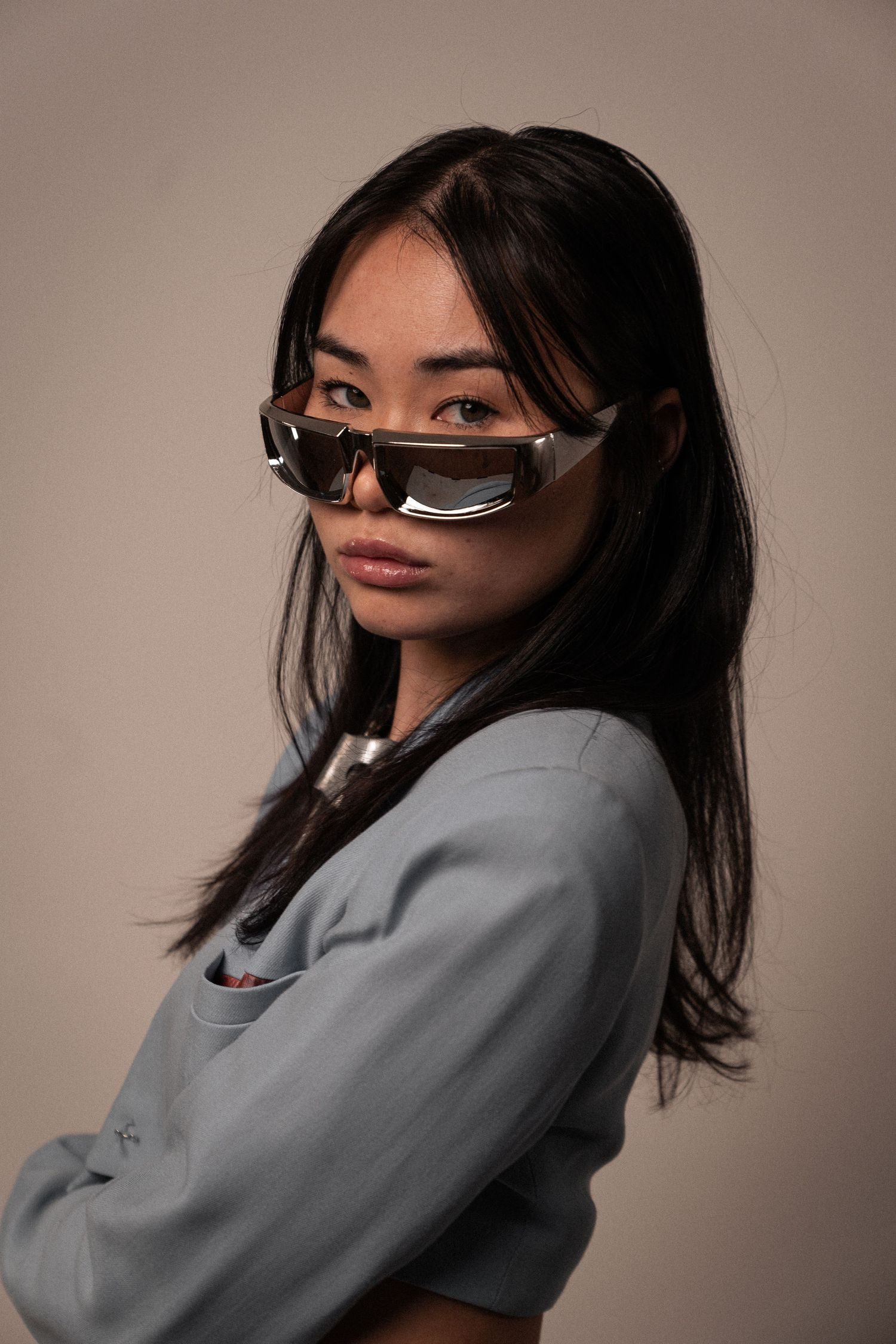 A woman in a grey blazer and dark sunglasses, looking back over her shoulder.